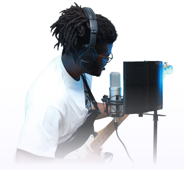 Musician with dreadlocks wearing headphones and glasses, playing an electric guitar and singing into a studio microphone with a pop filter.